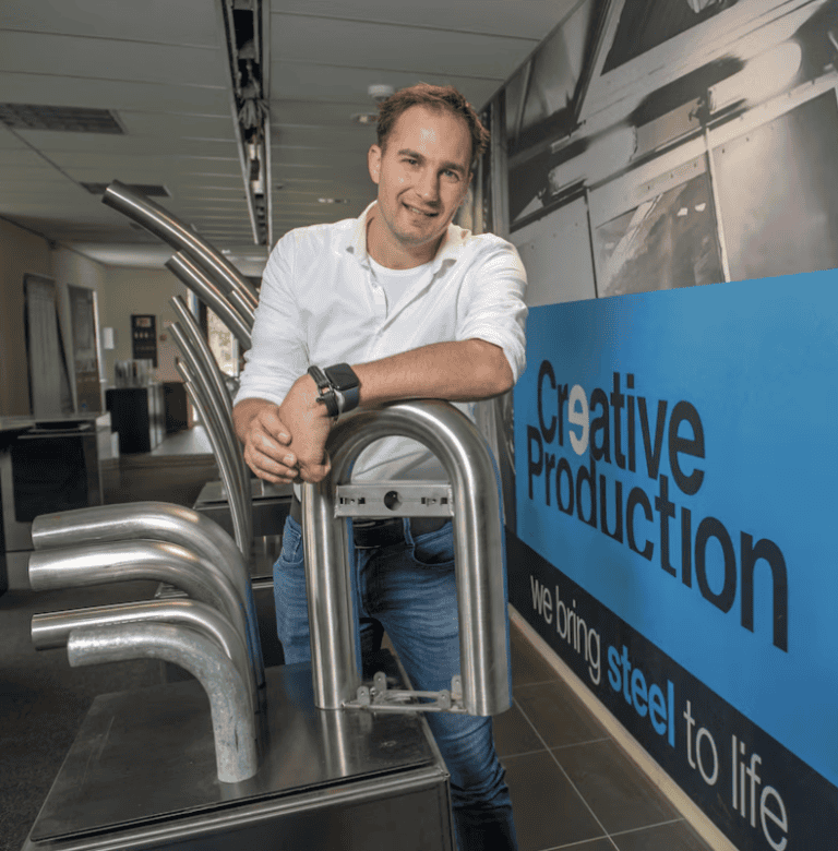Man bij staalkunstwerk in creatieve productieomgeving, focus op staalconstructies.
